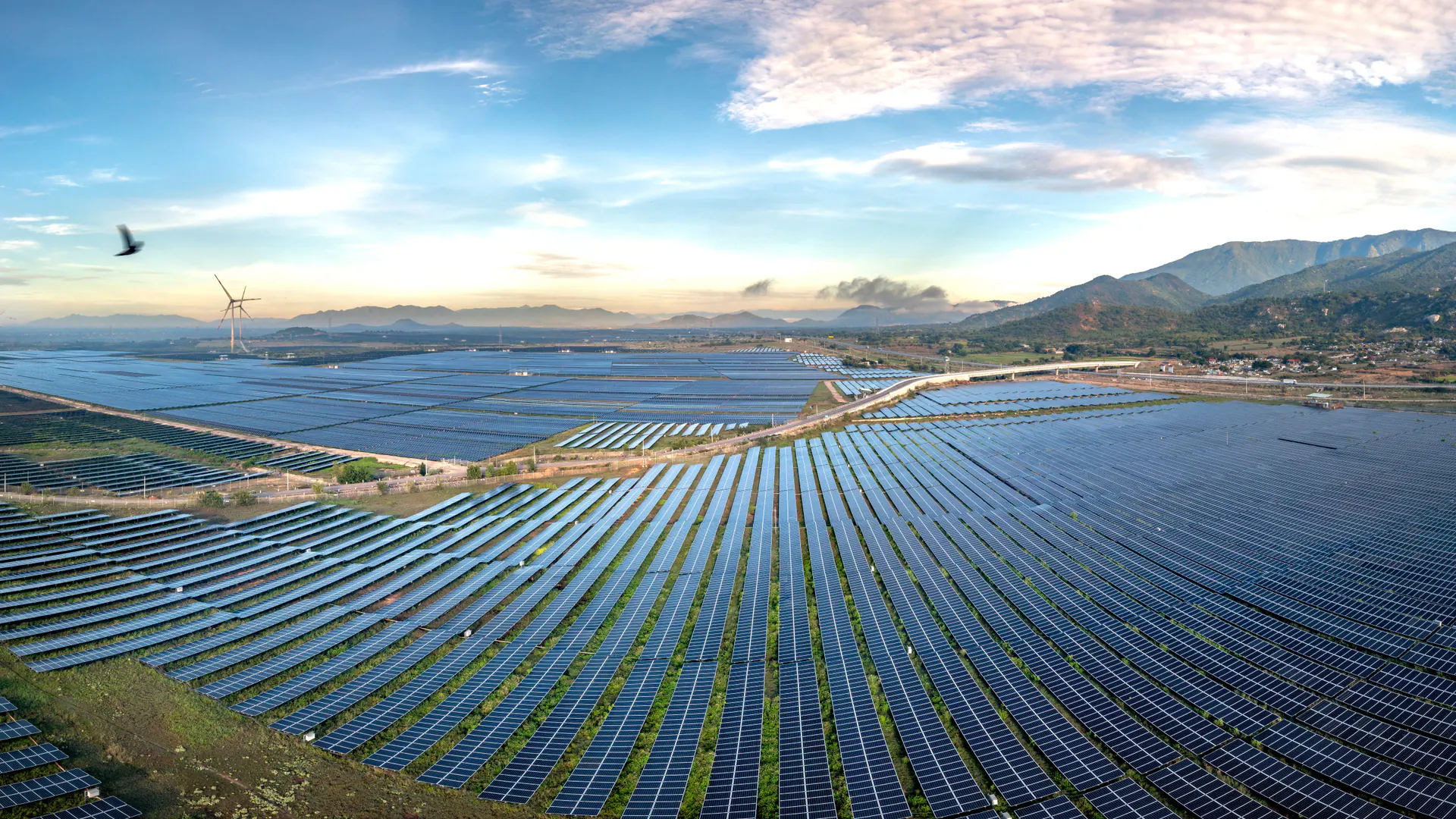Rows of photovoltaic panels across a large solar installation with surrounding hills